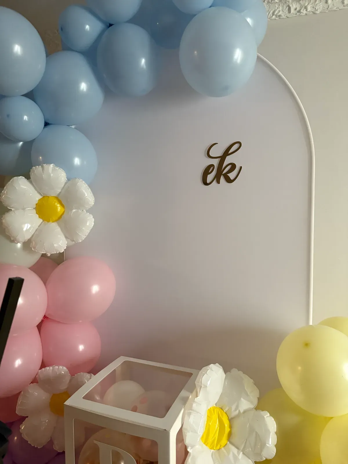Pastelowa ścianka balonowa z balonami-stokrotkami i złotymi inicjałami