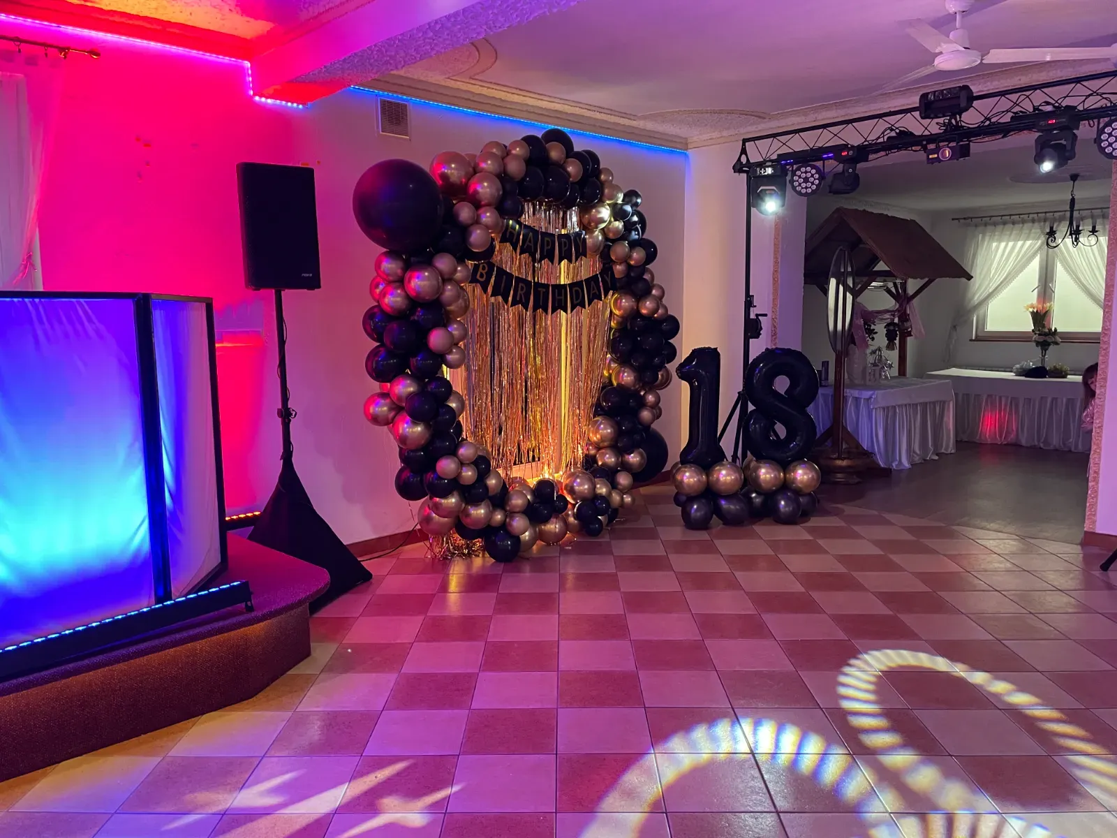 Ścianka balonowa z cyfrą 18 obok stanowiska DJ-a w różowym świetle