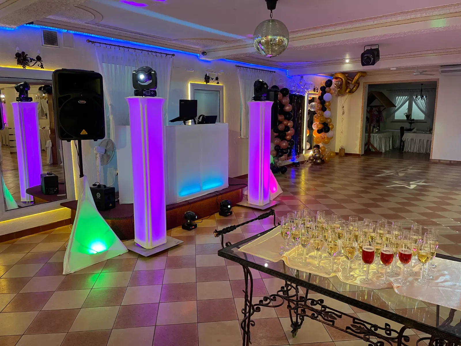 Stanowisko DJ-a z podświetlanymi kolumnami i tacą kieliszków szampana