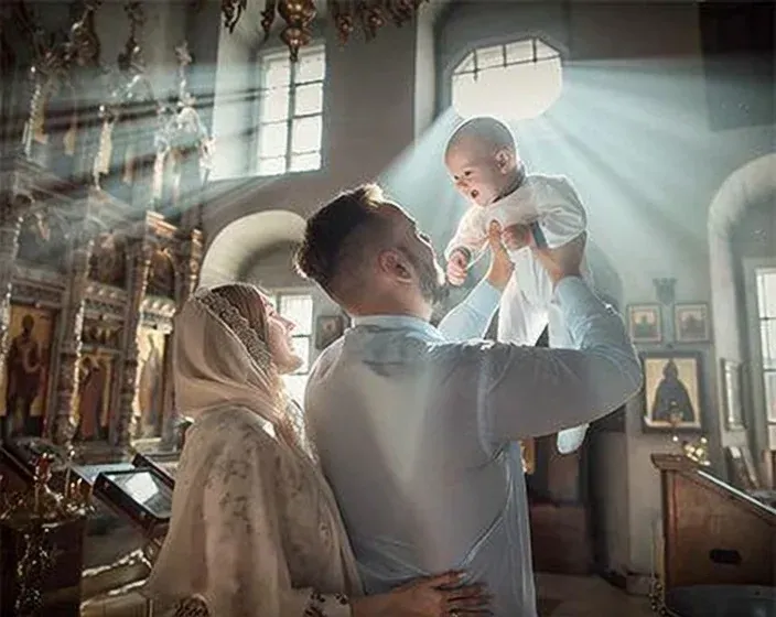 Chrzest — rodzice unoszą dziecko w promieniu światła